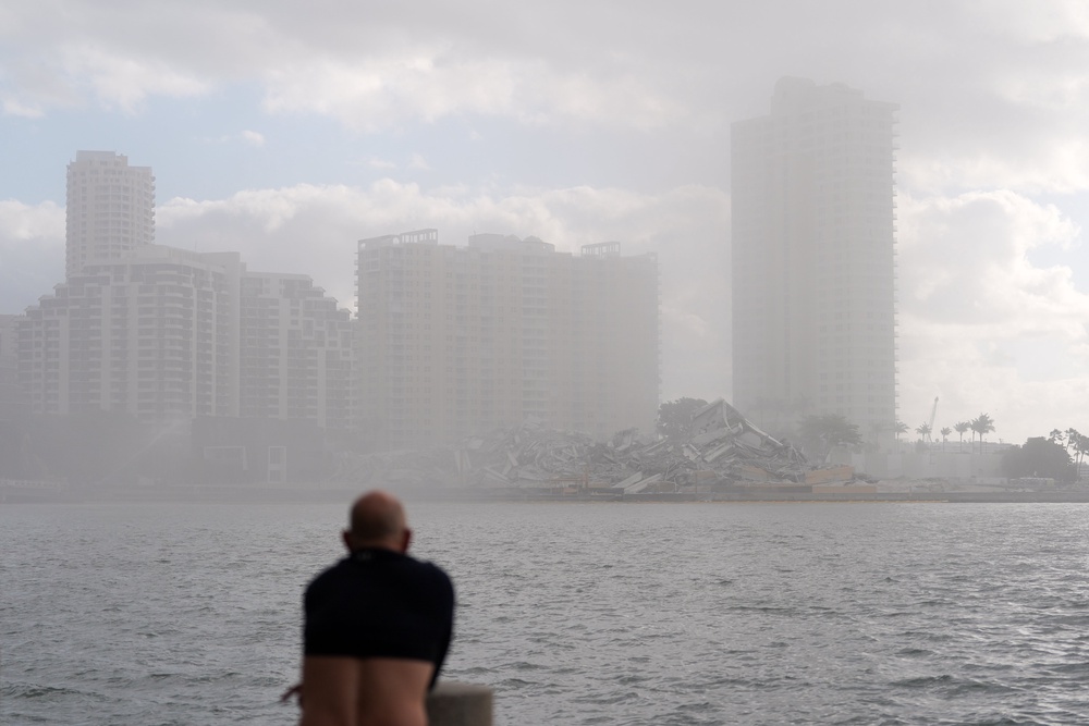 A man, with his shirt pulled up to cover his nose against dust, looks toward the debris following the controlled implosion (AP)