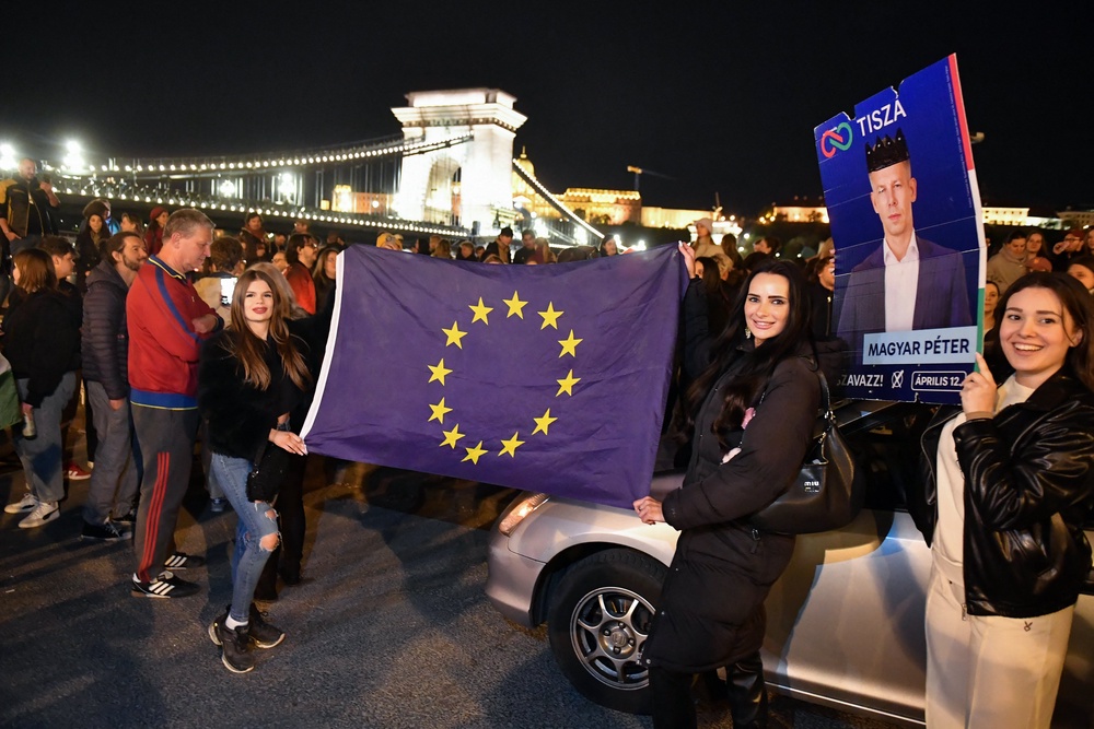 Participants display an election campaign poster of Hungary's prime minister-elect, Peter Magyar and a flag of the European Union during a spontaneous gathering to celebrate the victory of the conservative Tisza party near the Szechenyi Chain Bridge in Budapest (AFP/Getty)