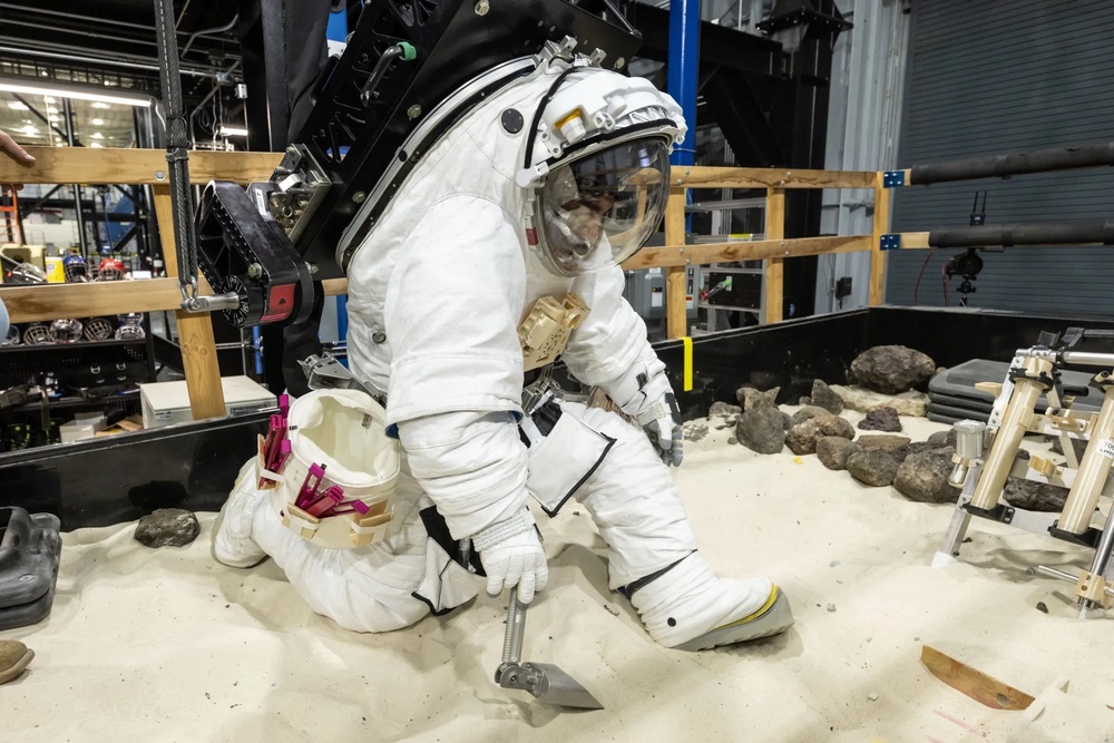 A NASA crew member practices using lunar tools to collect geology samples at NASA’s Johnson Space Center during a pressure test in an Artemis III lunar spacesuit developed by Axiom Space (NASA/Bill Stafford)