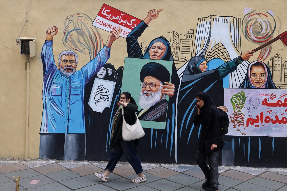 People walk past an anti-USA and anti-Israel mural depicting the late Iranian supreme leader Ayatollah Ali Khamenei, in Tehran on 21 April (AFP/Getty)