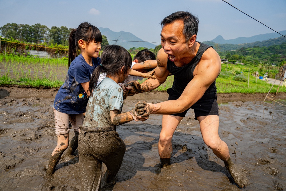 A man joins children in a mud wrestling activity in a muddy field during an organised event, involving mud races and wrestling matches, in Hong Kong on 18 April 2026 (AFP/Getty)