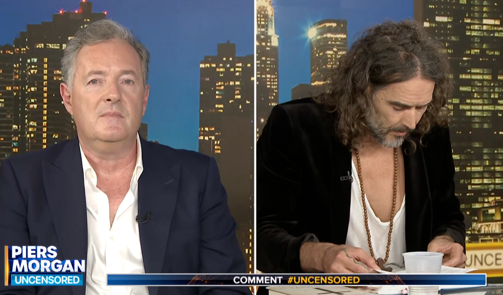 Piers Morgan awkwardly looks at the camera as Russell Brand struggles to find a Bible passage (Piers Morgan: Uncensored)