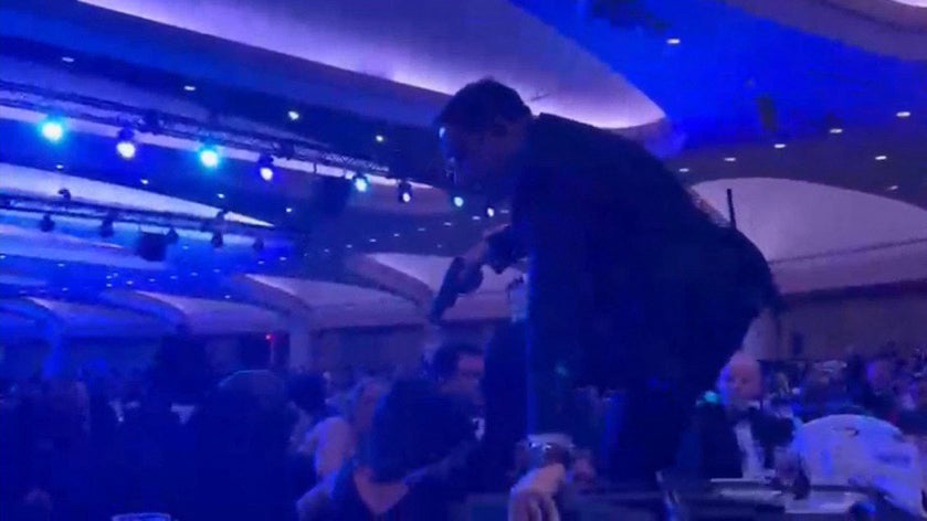 A screen grab taken from a video filmed by an AFP reporter shows an armed agent climbing over chairs as they move to the stage after loud bangs were heard during the White House Correspondents' dinner at the Washington Hilton in Washington, DC, on April 25, 2026. (AFP/Getty)