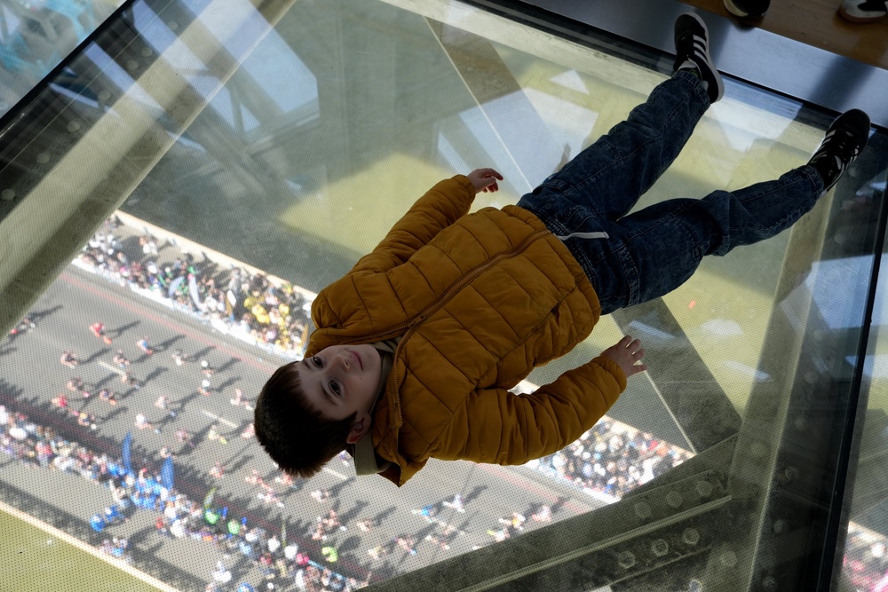 A child lies on the glass floor of Tower Bridge as runners cross underneath (Jonathan Brady/PA) (PA Wire)