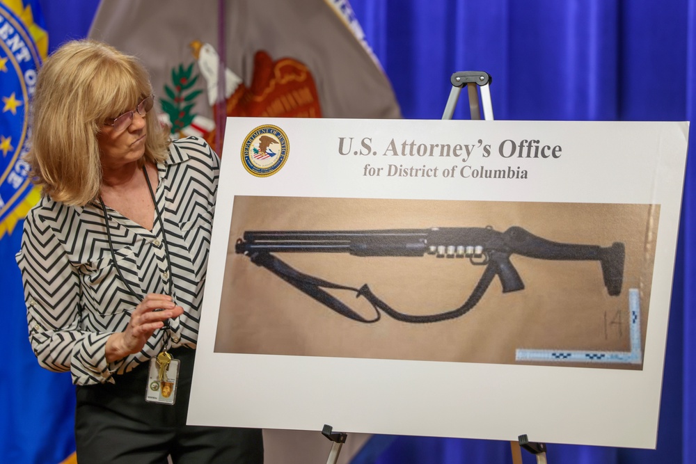 A Justice Department staffer displays a photo of the shotgun Cole Allen allegedly used in a planned assassination of President Donald Trump (Getty)