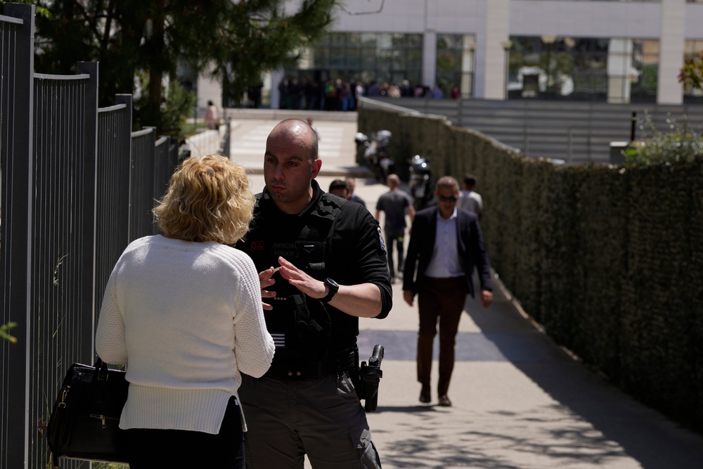 A policeman speaks with a woman outside a courthouse after a gunman opened fire, leaving several people wounded in Athens, on Tuesday, 28 April 2026 (AP)