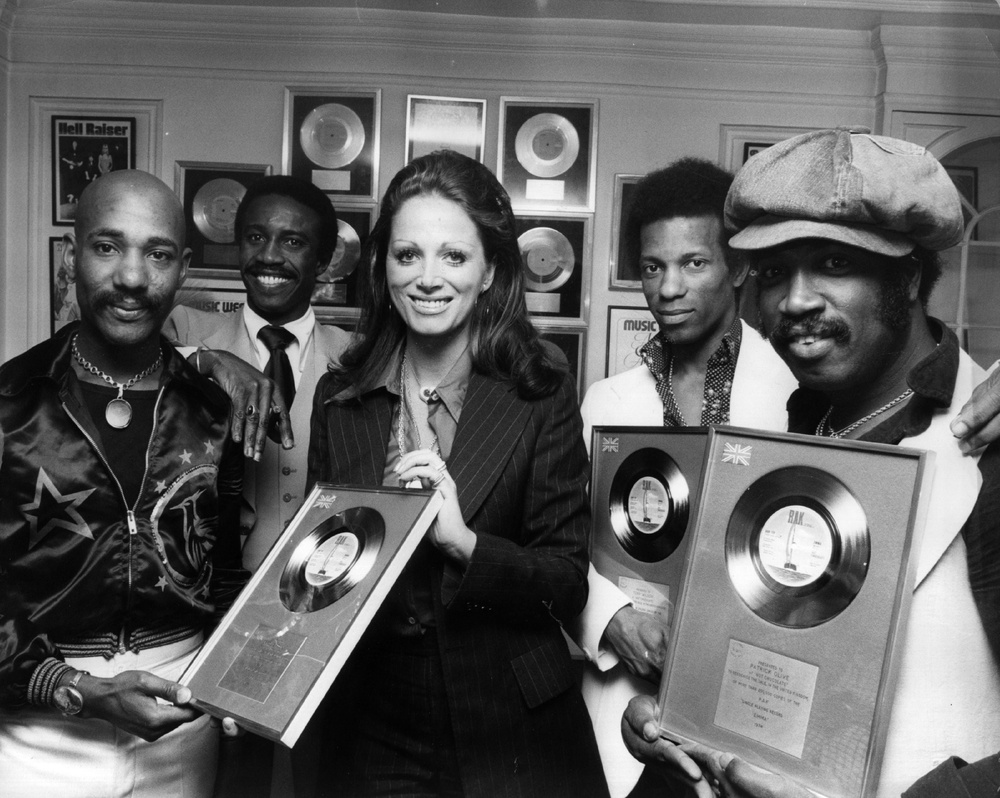 Errol Brown, Larry Ferguson, Tony Wilson and Patrick Olive of Hot Chocolate being presented with silver discs by Jackie Collins after their song 'Emma' reached number two in the British charts (Getty)