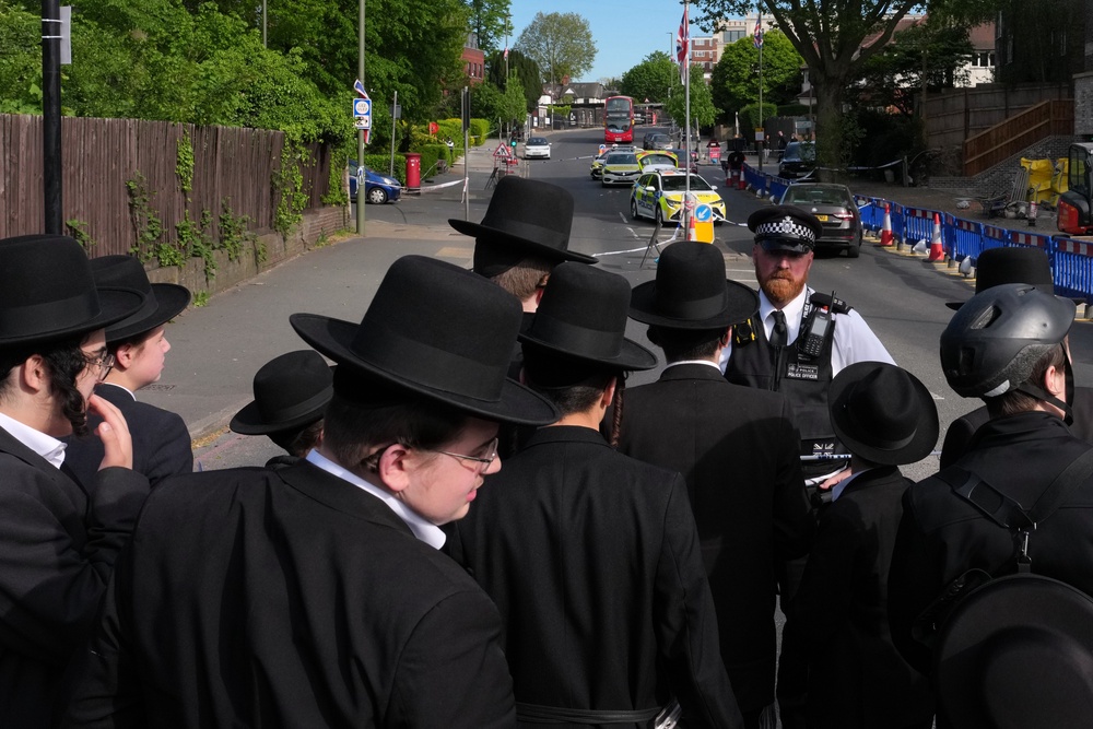 Members of the community watch as forensic officers search the area (AP)