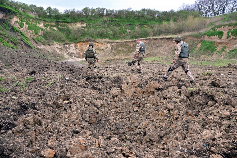 Deminers of the Ukrainian Emergency Service walk past a crater following the explosion of anti-tank mines and other weapons, found in the town of Bucha (AFP/Getty)