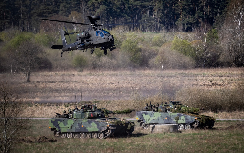 A Dutch Boeing AH-64 Apache attack helicopter flies over 2 Swedish Stridsfordon 90 tracked armoured combat vehicles as the Nato allies take part in a combat display during press day for the military exercise Aurora 26 at the Revingehed training field outside Lund in Skane, Southern Sweden on 29 April 2026 (AFP/Getty)