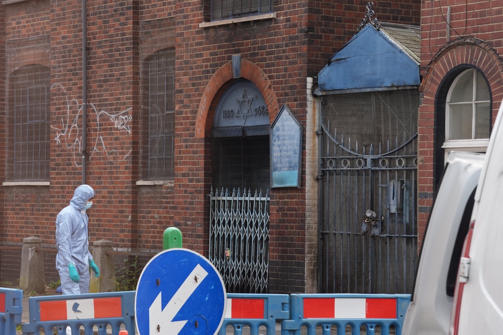 A forensic investigator looks at the fire damaged gates at the entrance to the former East London Central Synagogue (Lucy North/PA) (PA Wire)