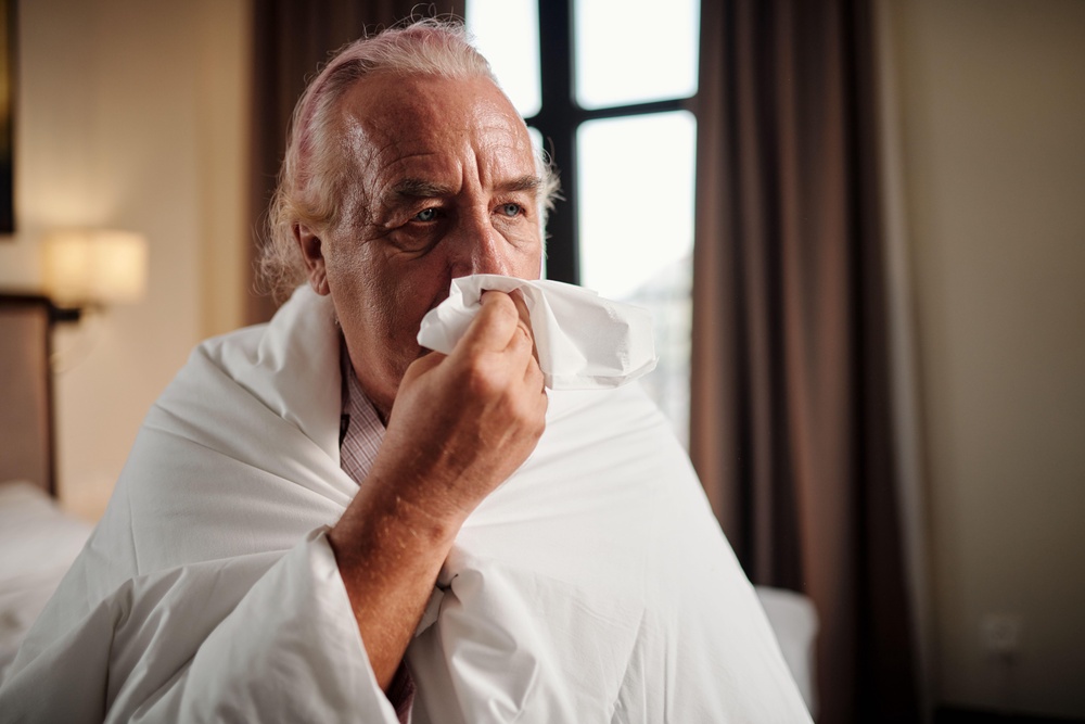 A man wrapping in a duvet blowing his nose with a tissue (Alamy/PA)