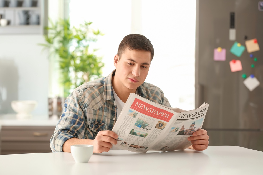 Teenage boy reading newspaper in kitchen (Alamy/PA)