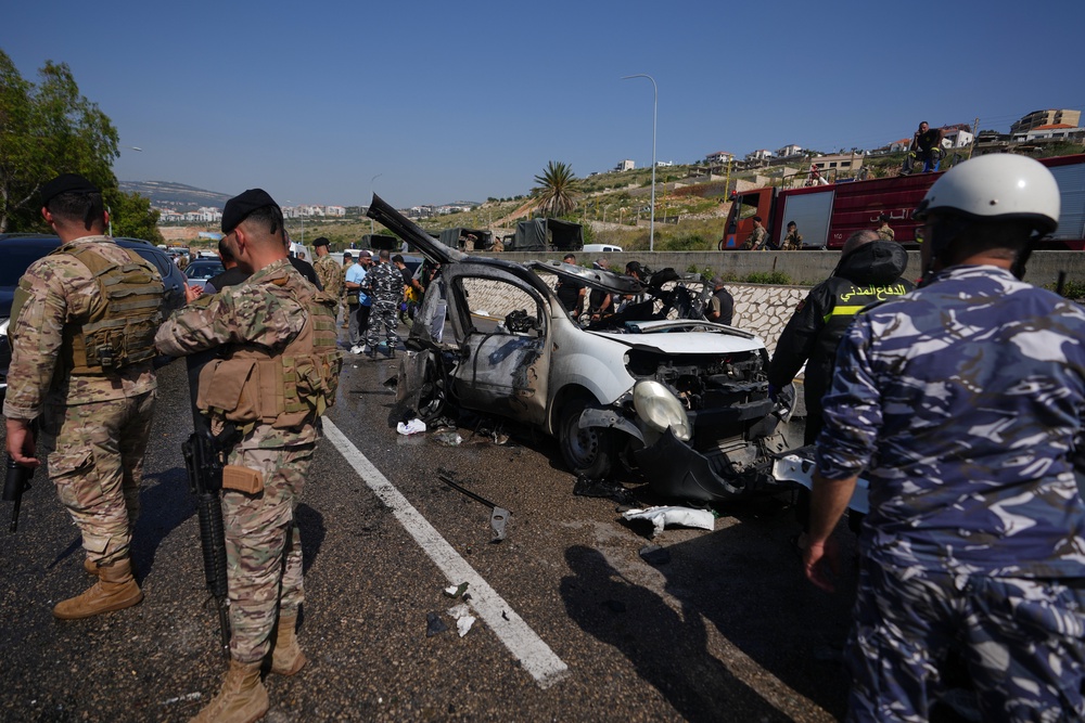 Security forces and emergency responders gather around a damaged vehicle at the scene of an Israeli airstrike that hit a car in the coastal town of Saadiyat, south of Beirut (Associated Press)