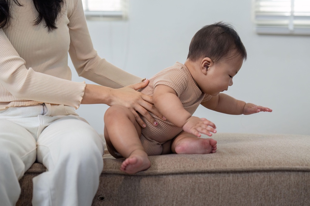 Mother helping baby sit up (Alamy/PA)