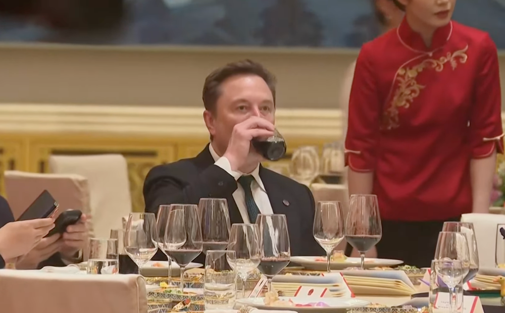 Musk taking a swig of a red drink (The Independent)