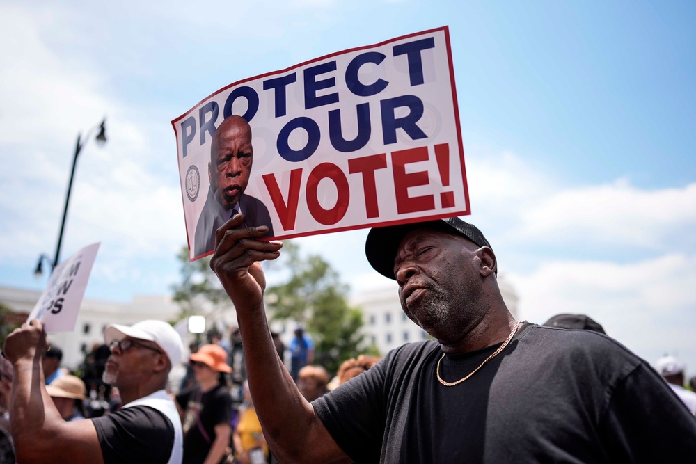 Rally-goer Aaron McGuire holds a poster with the image of the late Rep. John Lewis, the influential civil rights activist who led a march from Selma to Montgomery in 1965 (AP Photo/Mike Stewart)