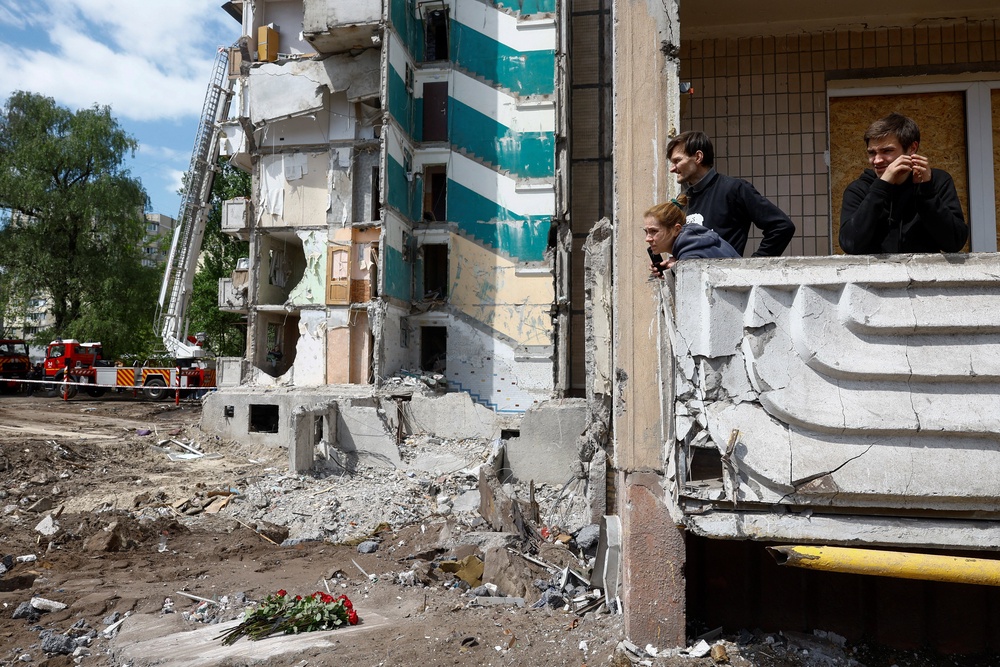 Residents stand on a damaged balcony of their apartment and look at the site of a neighbouring apartment building where 24 residents were killed (REUTERS)
