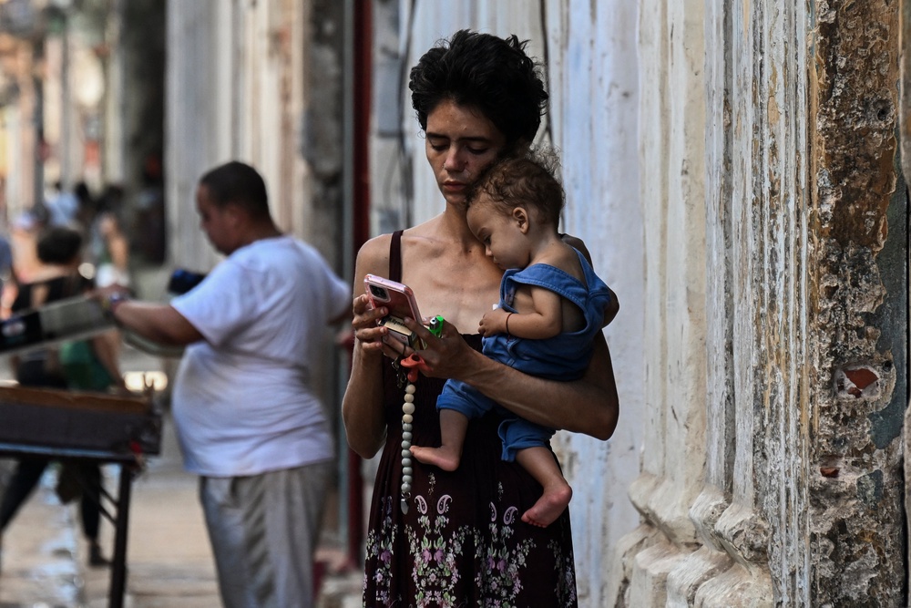 A woman carries her baby while looking at her mobile phone in Havana on May 20, as the island continues to face food shortages and blackouts (AFP/Getty)