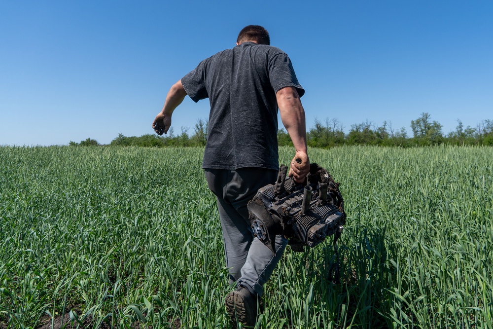 A farmer carries a fragment of a Russian drone on an agricultural field near the front line in the Kharkiv region, Ukraine, Friday, May 22, 2026 (AP Photo/Andrii Marienko)