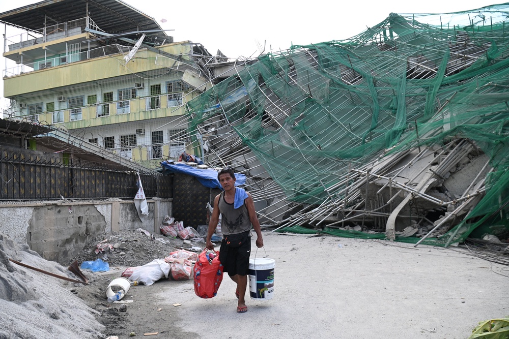A worker carries belongings retrieved from a collapsed building in Angeles City on 25 May 2026 (AFP/Getty)