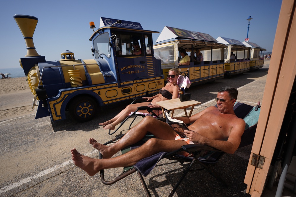 A couple sunbathe as the land train drives past on Bournemouth promenade (Andrew Matthews/PA) (PA Wire)