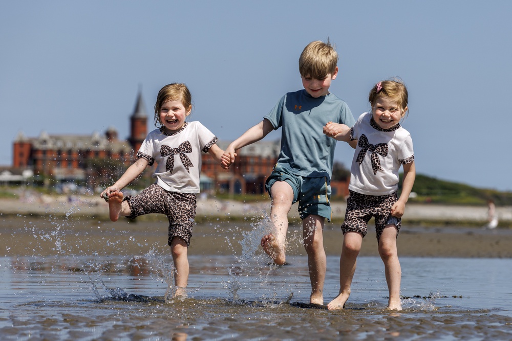 From left, Kara, Conor, and Katie McLaughlin make a splash on Newcastle beach in Co Down (Liam McBurney/PA) (PA Wire)