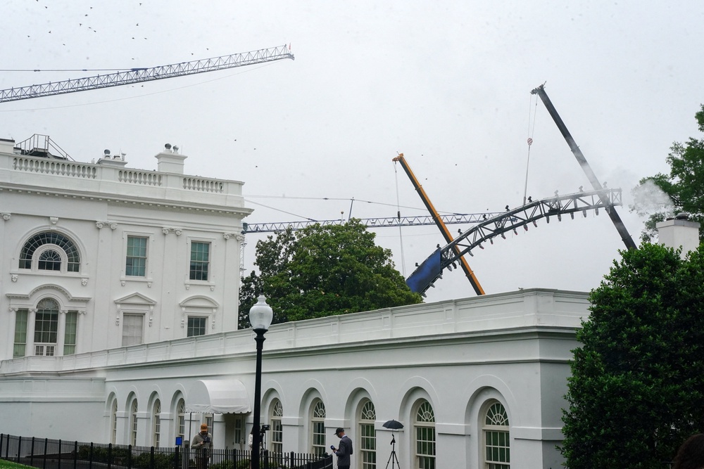 In one photo taken Monday, cranes can be seen carrying a section of the rig as it arches in front of the White House (Reuters)