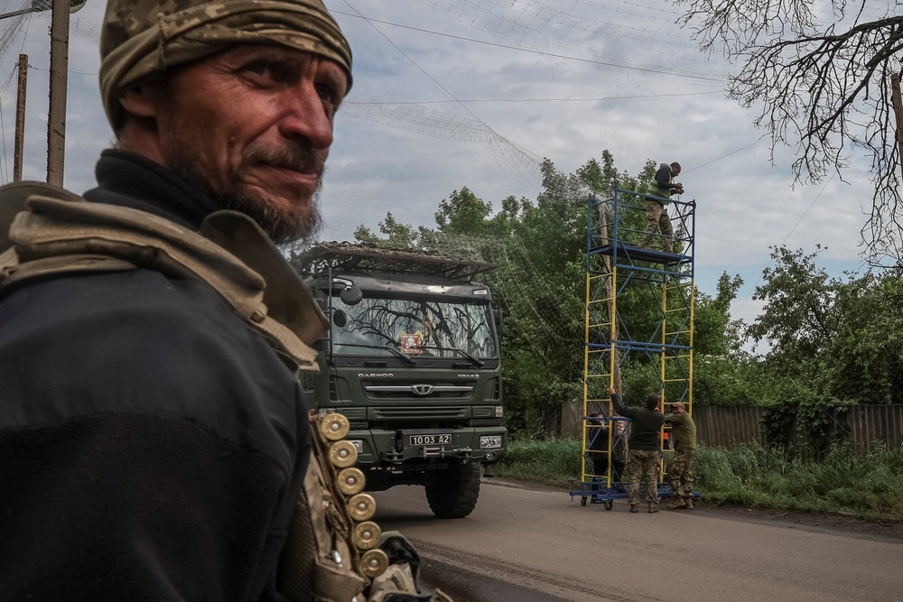 A military truck passes workers and service members installing anti-drone nets over a road in Donetsk region (Reuters)