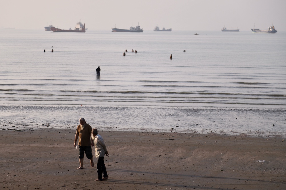 Men walk on the shoreline as people wade in the water in the Strait of Hormuz, where cargo and service vessels are anchored off Bandar Abbas, Iran (Amirhosein Khorgooi/ISNA via AP) (AP)