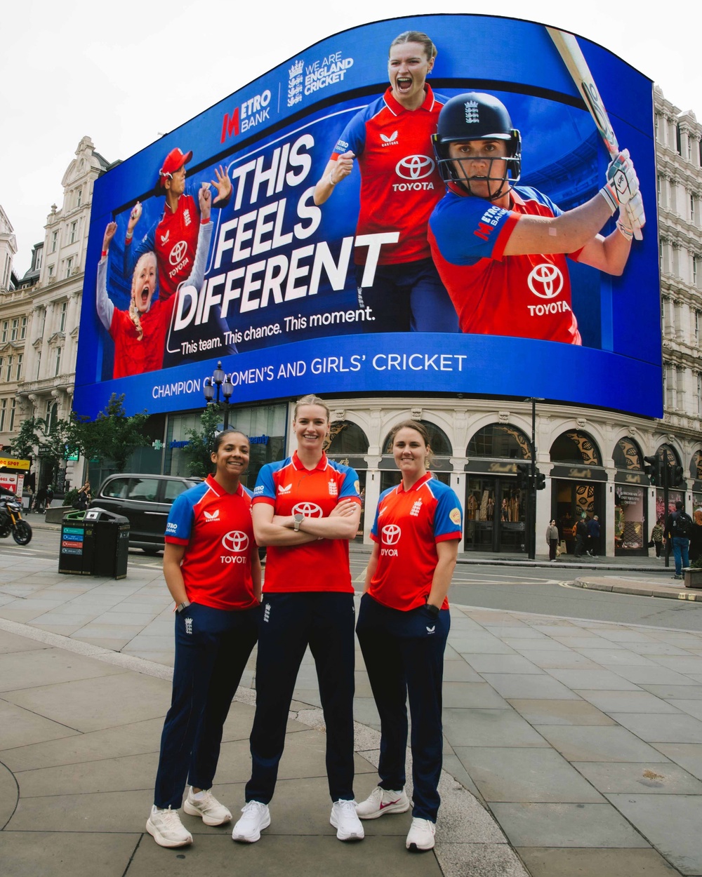England cricketers Sophia Dunkley, Lauren Bell and Nat Sciver-Brunt in front of Piccadilly Lights (Handout/Metro Bank)