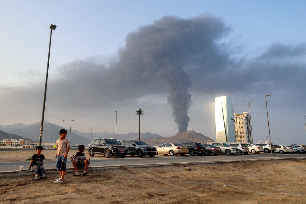 Boys sit on the side of a road watch as a tall smoke plume billows following an explosion in the Fujairah industrial zone in the UAE earlier this year (AFP/Getty)