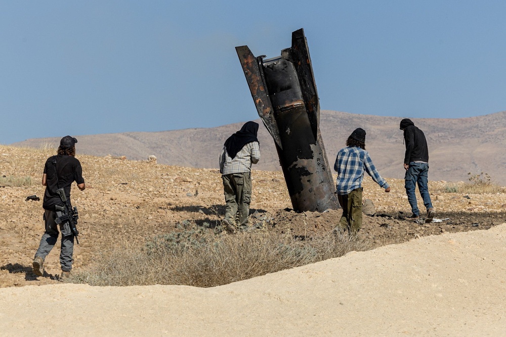 Israeli settlers stand next to part of a missile protruding from the ground, following strikes from Iran, in the central Israeli-occupied West Bank, 8 June 2026 (Reuters)