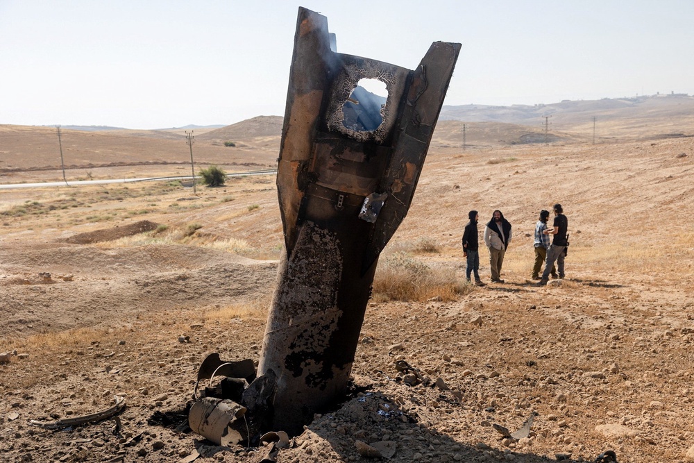 Israeli settlers stand next to part of a missile protruding from the ground, following strikes from Iran, in the central Israeli-occupied West Bank, 8 June 2026 (Reuters)