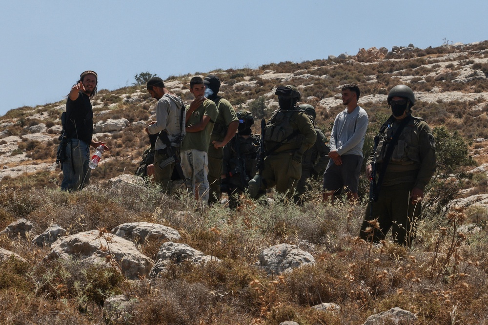Israeli forces and armed settlers guard a bulldozer reportedly operating on Palestinian land on 9 June (AFP/Getty)