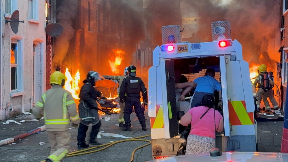 People seek safety in a police van as fires break out in a residential street (PA)
