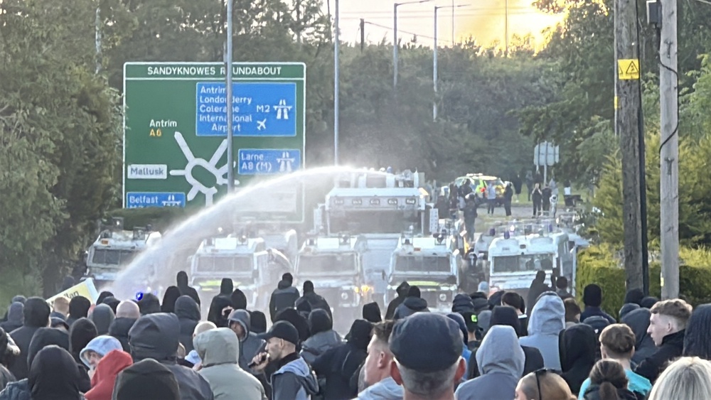 A water cannon is fired towards protesters on Antrim Road, at the Sandyknowes roundabout in Newtownabbey (PA) (PA Wire)