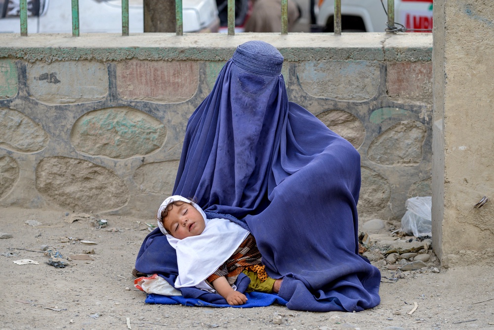 An Afghan burqa-clad woman carrying a child seeks alms along a road (AFP/Getty)