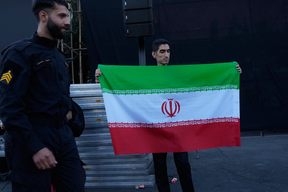 A man holds an Iranian flag while a policeman walks past at the Islamic Revolution square in Tehran, Iran, Sunday, June 14, 2026 (AP)