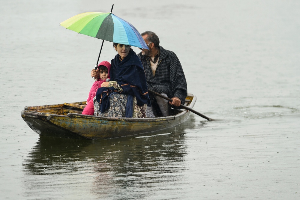 A Kashmiri woman shelters from the rain under an umbrella with a child while a man paddles a boat along Dal Lake in Srinagar (AFP/Getty)