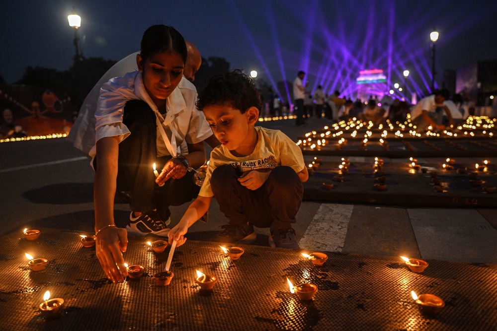 People light diyas, or traditional earthen oil lamps, as a drone laser show is organised at the India Gate memorial as part of the Diwali celebrations, the Hindu festival of lights, at Kartavya Path in New Delhi on 18 October 2025 (AFP/Getty)