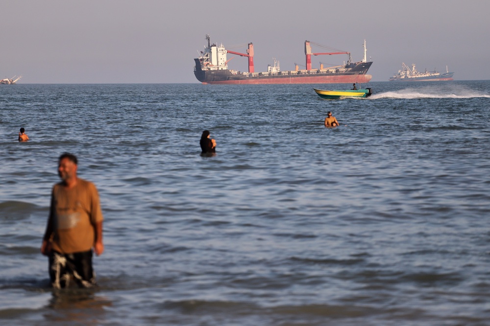 Residents swim in the waters of the Strait of Hormuz as a small motorboat passes cargo ships and other commercial vessels offshore near Bandar Abbas, Iran, Wednesday, 17 June 2026 (AP)