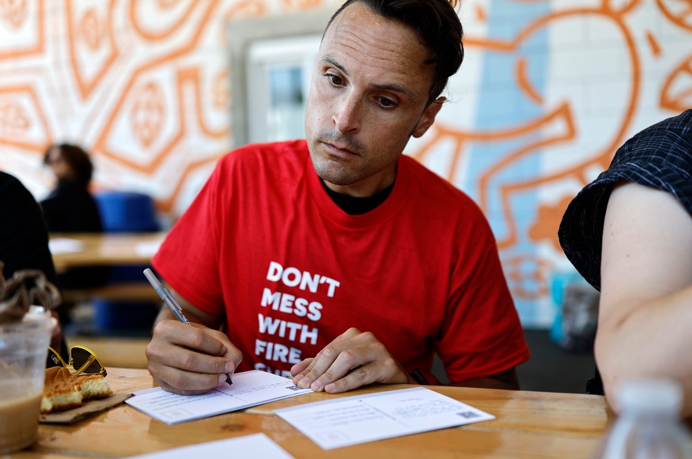 A man writes a postcard as part of a campaign by the Eaton Fire Survivors Network in Altadena, California, in July 2025. Writing by hand requires focus, intention and can be therapeutic (Getty Images)