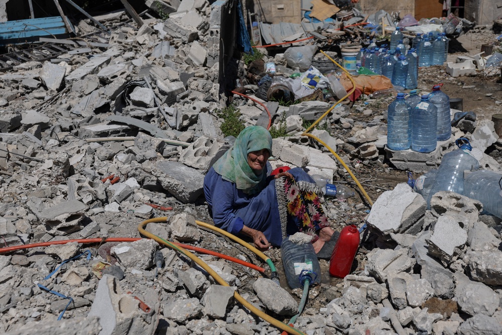 Khadija Amara, whom local residents said had not left her home, fills a jerrycan with water as she sits among the rubble of a house, which was damaged by an Israeli strike, in Qlaileh in the Tyre district, southern Lebanon (Reuters)