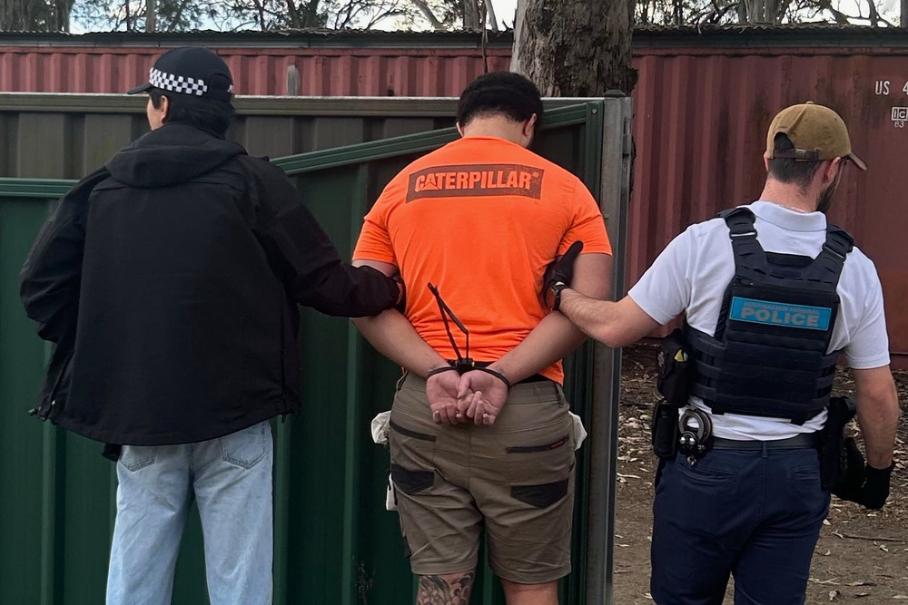 In this photo provided by the Australian Federal Police, a man, center, is arrested by police in Londonderry in western Sydney, Friday, June 19, 2026. (Australian Federal Police via AP)