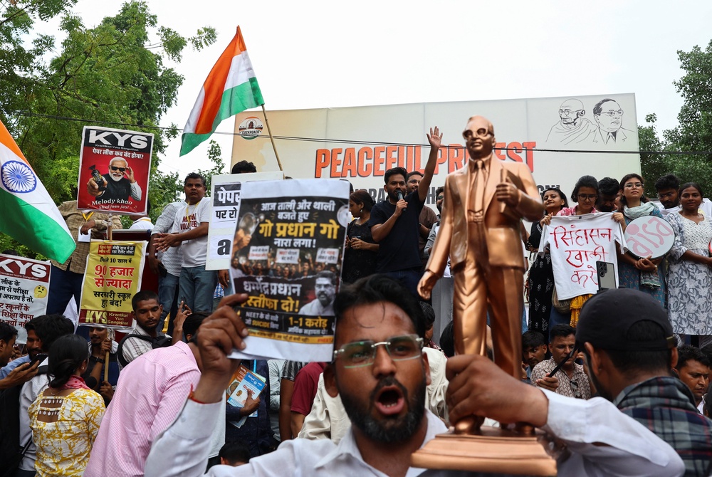 People hold placards and shout slogans as Abhijeet Dipke, head of the CJP, waves to the crowd during a sit-in protest demanding the resignation of Indian education minister Dharmendra Pradhan (Reuters)