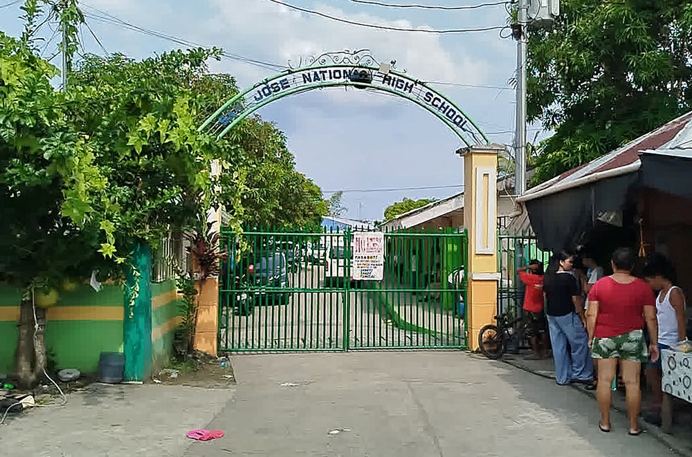 People stand next to the entrance gate of San Jose National High School after a shooting incident in Tacloban City, Leyte province on June 22, 2026 (AFP/Getty)