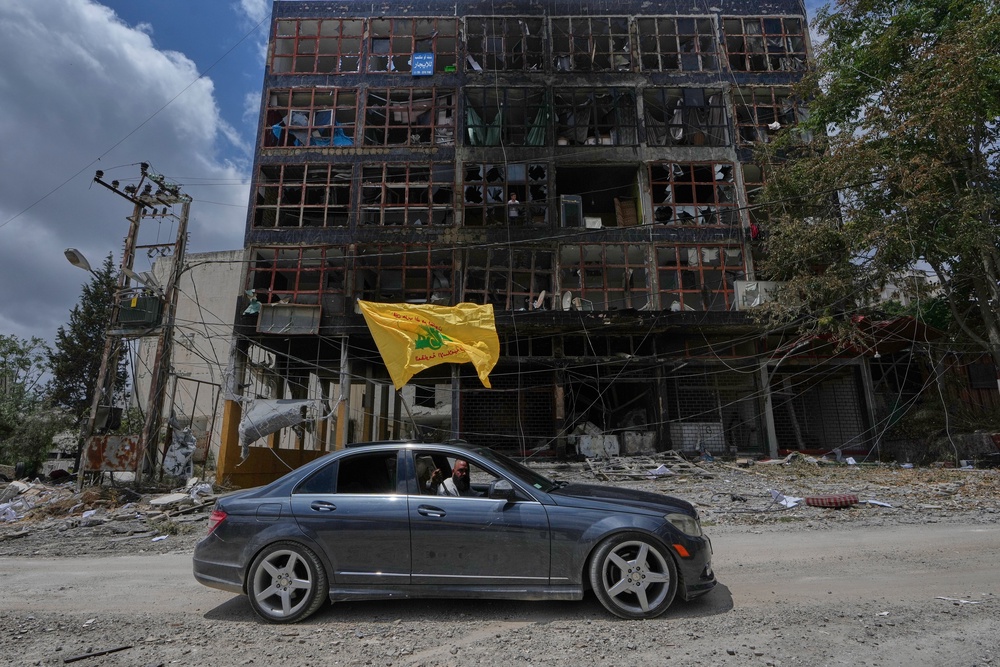 A man with a Hezbollah flag drives past a damaged building in Nabatiyeh, southern Lebanon, which has been devastated by Israeli airstrikes (AP)