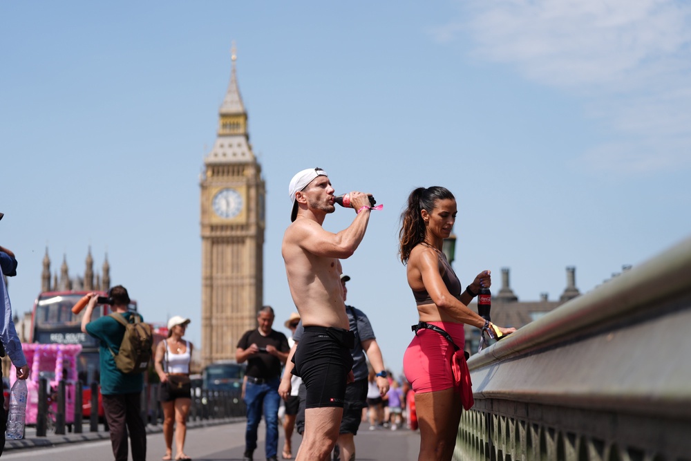 A topless man wearing a baseball cap backwards hydrates himself in the extreme heat (Ben Whitley/PA) (PA Wire)