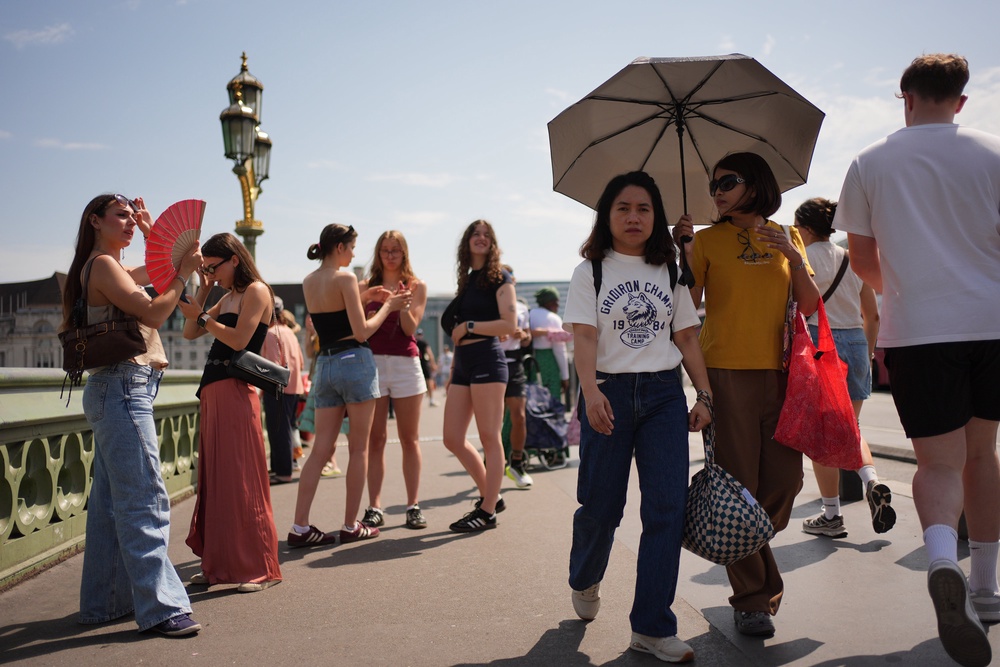 People sheltering from the sun under an umbrella on Westminster Bridge in central London (Yui Mok/PA) (PA Wire)